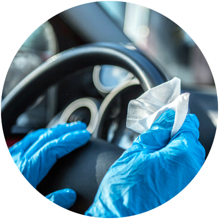 A gloved hand cleaning a steering wheel in a car