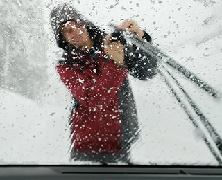Man adjusting a windshield wiper seen through an icy windshield.