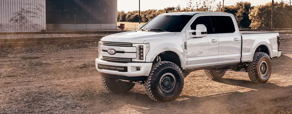 Large lifted white truck in a gravel lot.