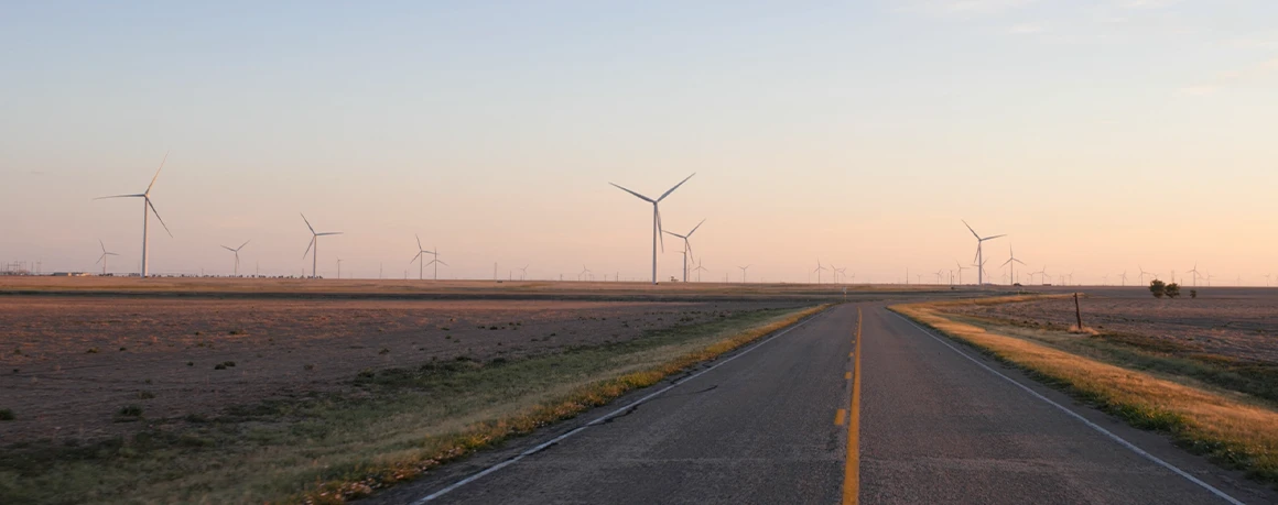 Driving along a lonely highway, wind turbines spin in the distance