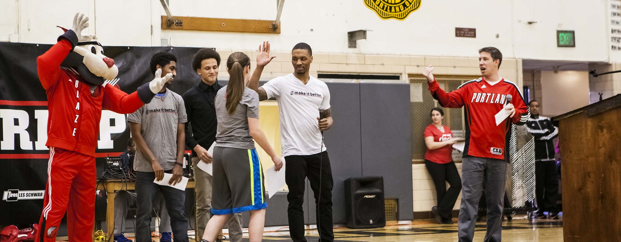 Damien Lillard high fives a student at Wilson High School as a Trailblazer mascot looks on.
