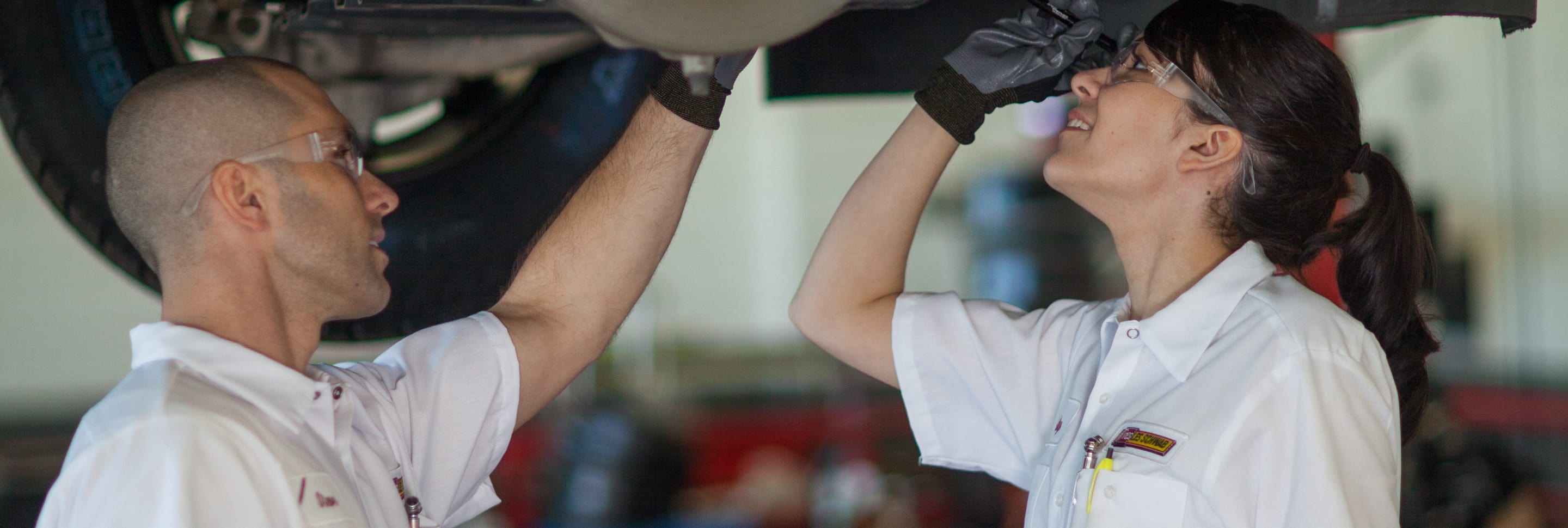 Two Les Schwab technicians examine one of the calipers of a car while it's on a lift.