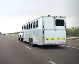 A trailer pulls a large horse trailer on the highway.