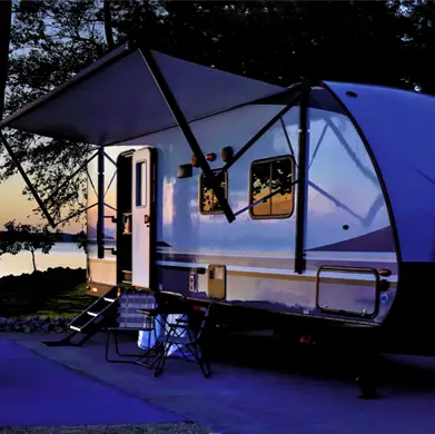 Travel trailer next to a lake at sunset.
