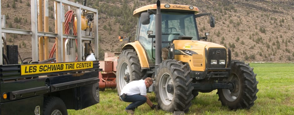 A Les Schwab technician repairing a tractor tire out at someon's farm.
