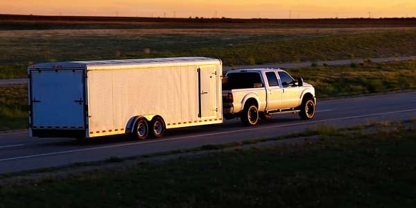 Pickup pulling long utility trailer at dusk