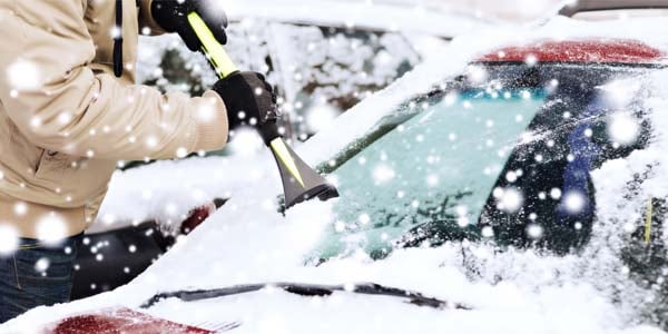 A man scraping ice from his car window.