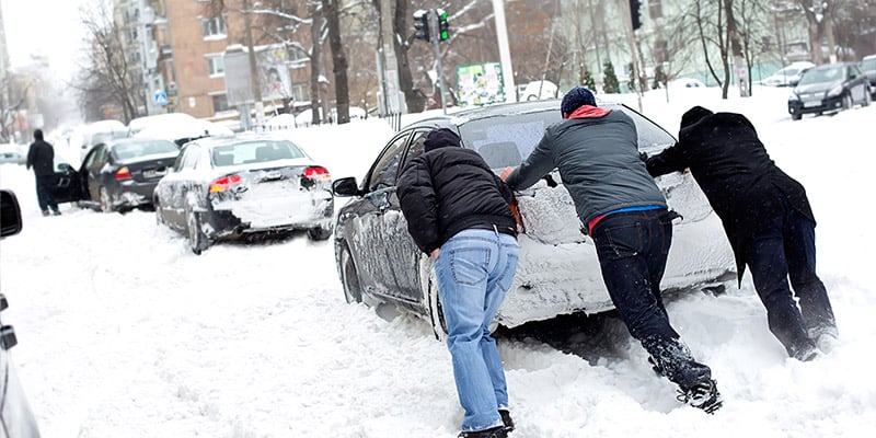 People pushing car out of snow