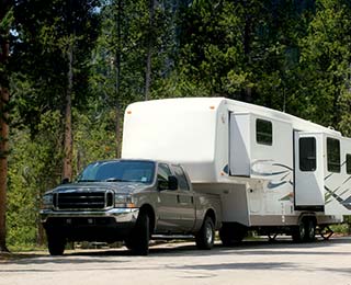 A truck and travel trailer parked in a forested campground.