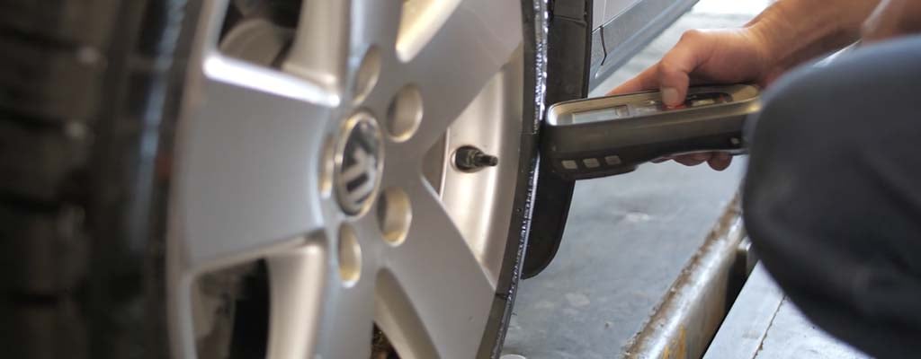 Tire technician resetting a TPMS monitor using a tool.