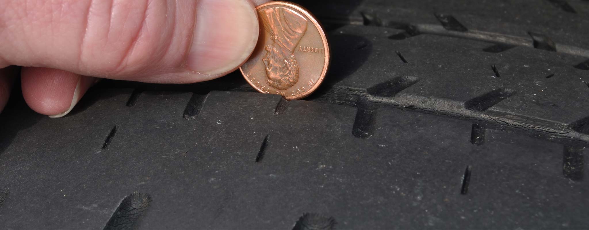 A person checking their tire tread deapth with a penny.