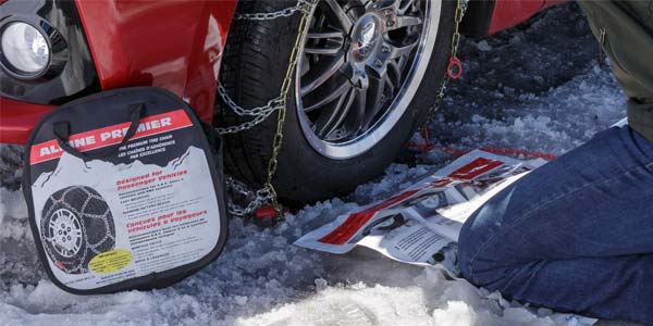 A person putting snow chains on their passenger car.