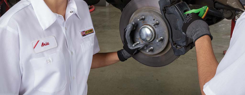 Two brake technicians using a gauge to measure break pad thickness