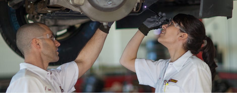 A pair of Les Schwab employees checking a vehicle's breaks while it sits on a post lift