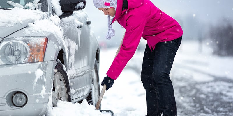 Woman digging stuck vehicle out of snow