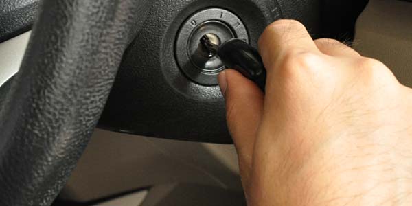 A hand putting a key in a car ignition.