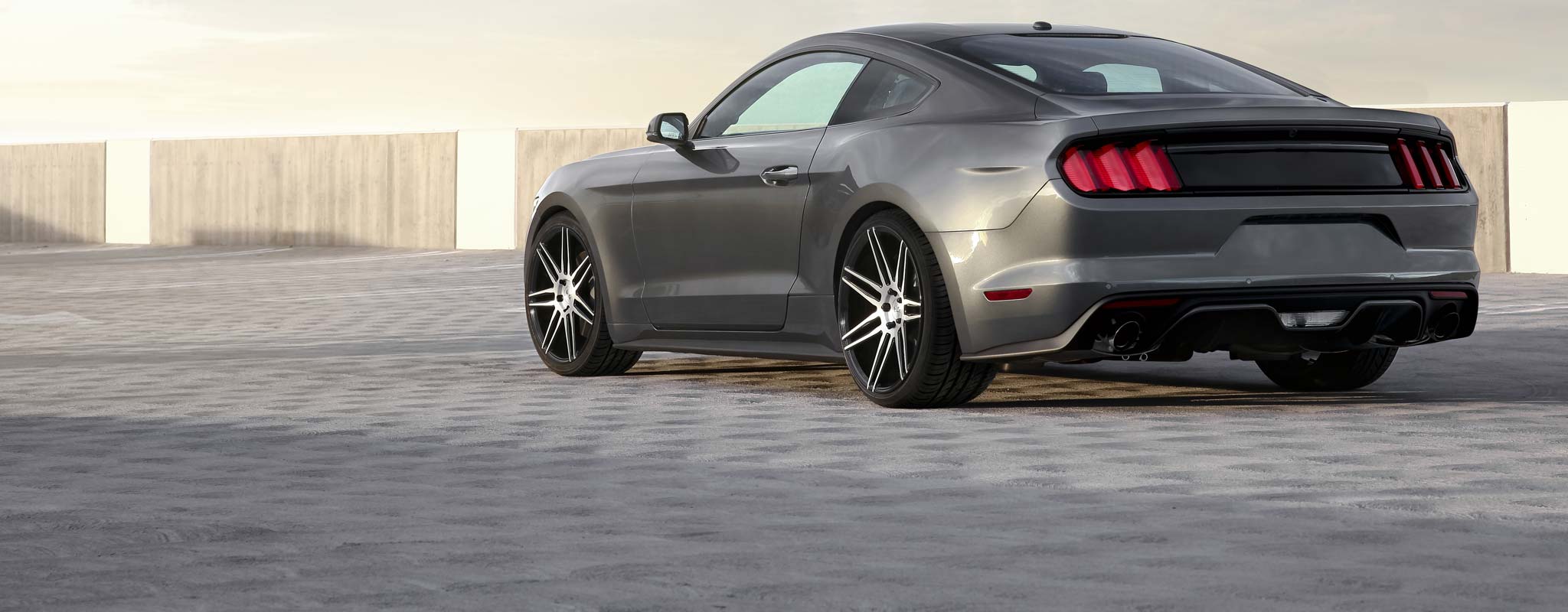 Grey Mustang parked on a cobblestone parking lot.