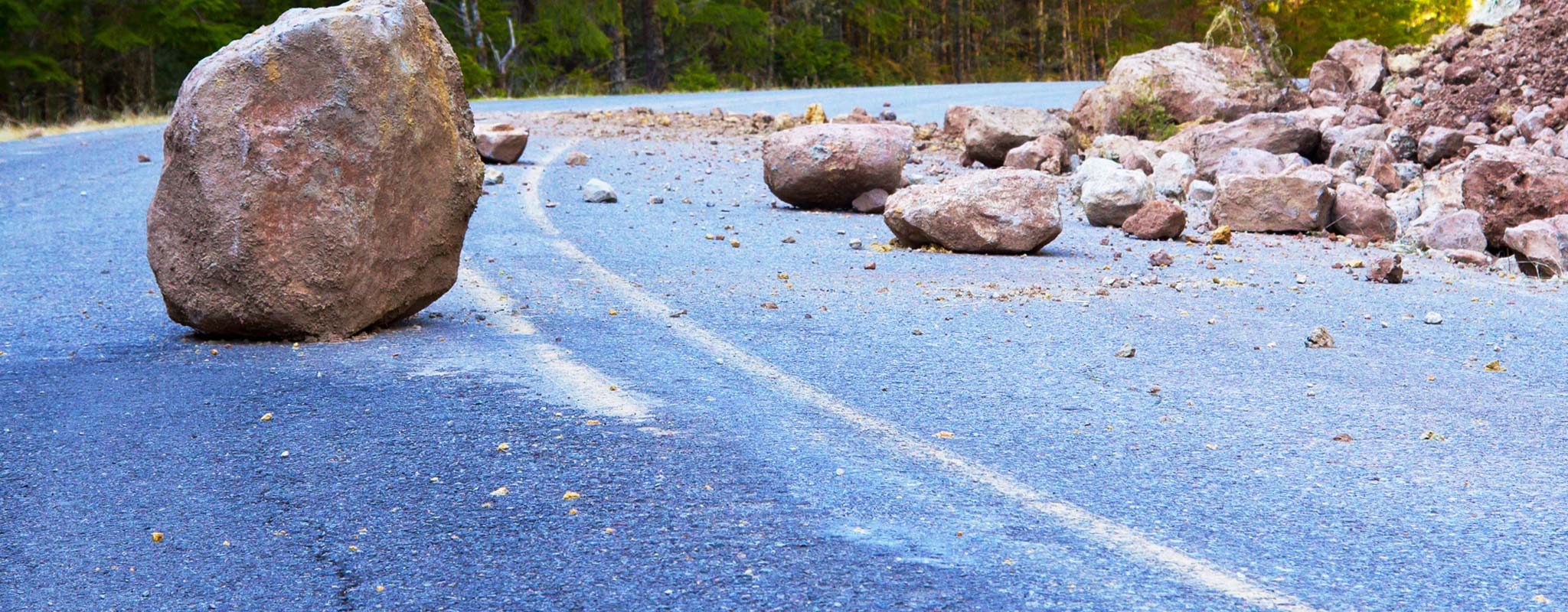 A rock slide with large boulders in the middle of a road.