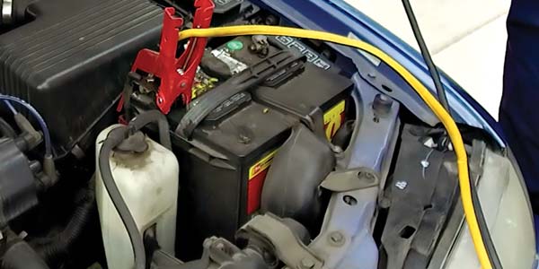 A car battery under the hood with jumper cables attached.