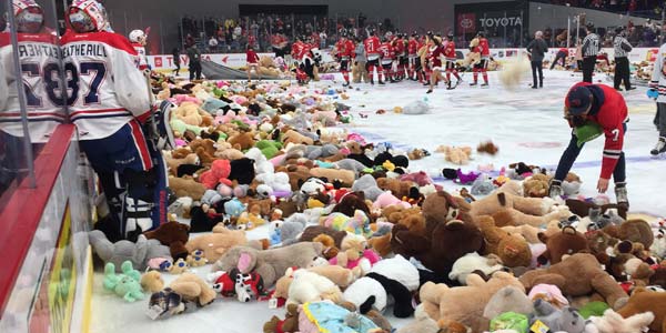 Ice rink full of hockey players and teddy bears after a teddy bear toss event.