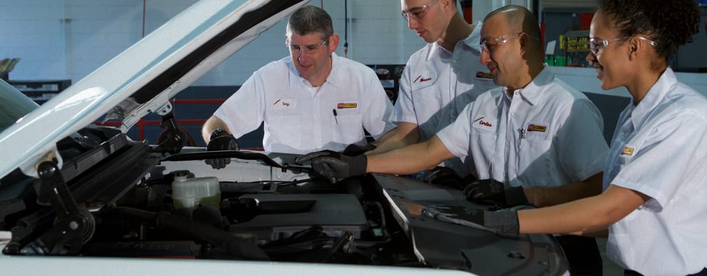 Four Les Schwab Employees Working Together On A Vehicle