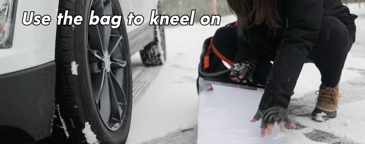 Person kneeling on tire sock bag to stay dry while installing tire socks