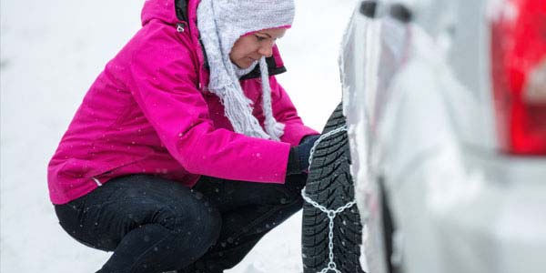 A woman putting chains on her snow tires.